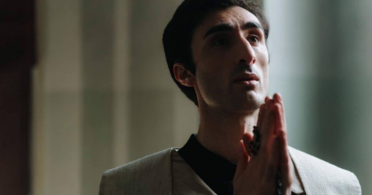 A priest deeply immersed in prayer inside a softly lit church, holding rosary beads.