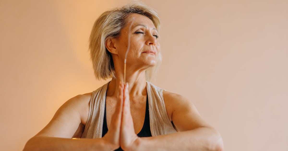 A senior woman meditating indoors with eyes closed, showcasing mental tranquility.
