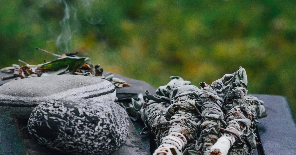 Herbal sage smudge and steaming hot stones on a wooden table in a natural outdoor setting.