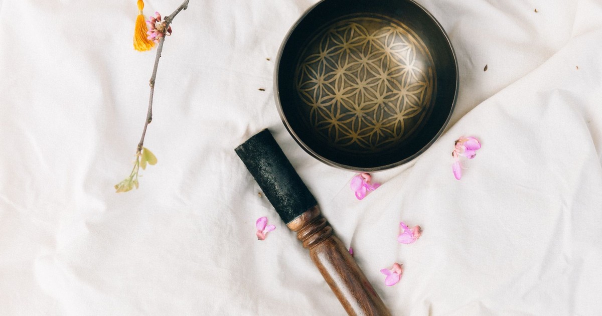 A Tibetan singing bowl on a white fabric surrounded by pink petals and branch, creating a serene atmosphere.