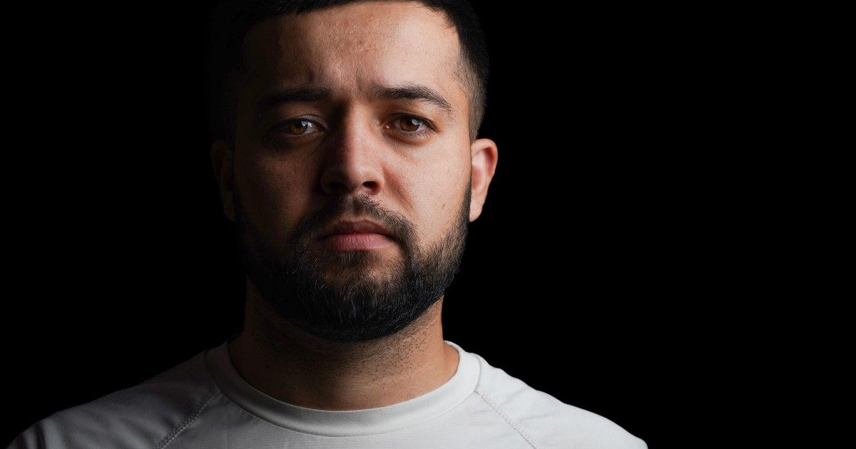 Studio portrait of a serious man with a beard in a white t-shirt against a black backdrop.