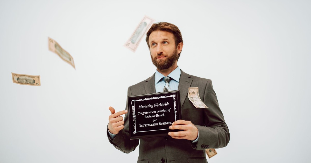 Businessman holding an award plaque, surrounded by falling cash, symbolizing success.