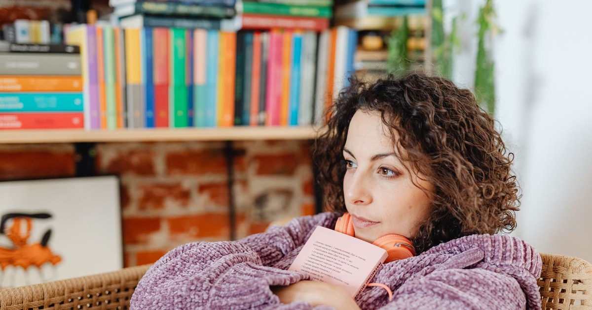 Woman relaxing with a book and headphones, surrounded by colorful bookshelves indoors.