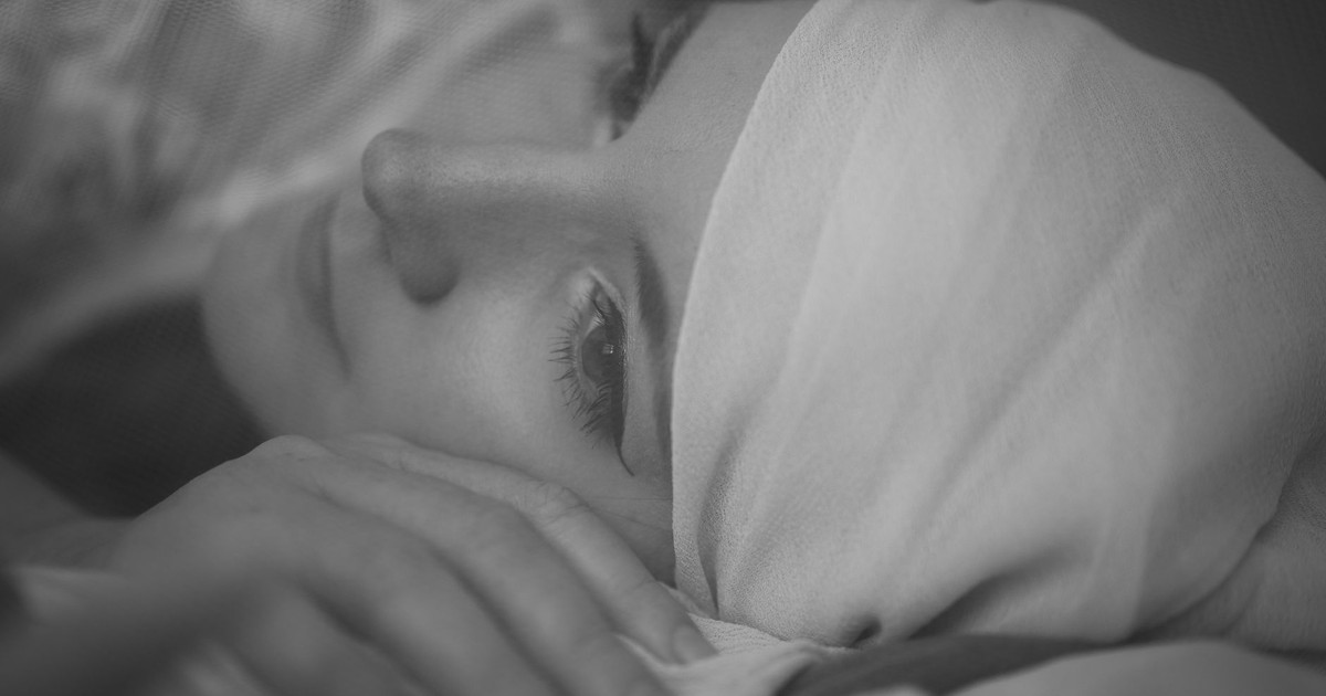 A serene black and white portrait of a woman lying down, wrapped in a headscarf, conveying a sense of tranquility.