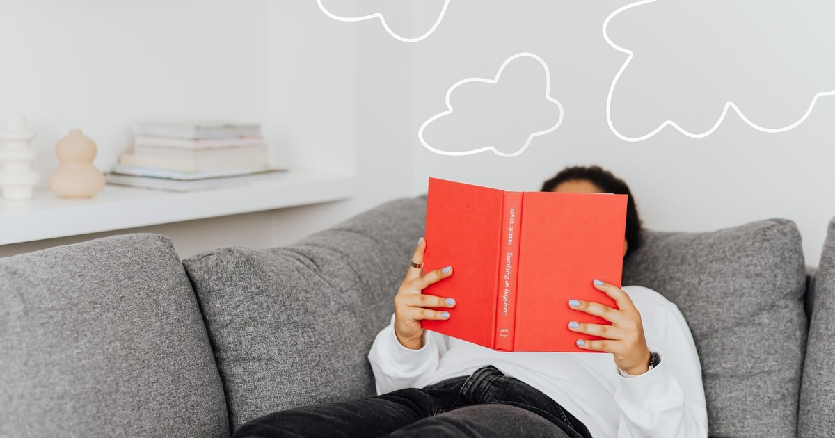Person relaxing with a book on a sofa. Drawn clouds add a whimsical touch.