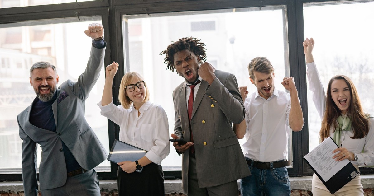 Group of diverse professionals celebrating achievement in office setting with enthusiasm.