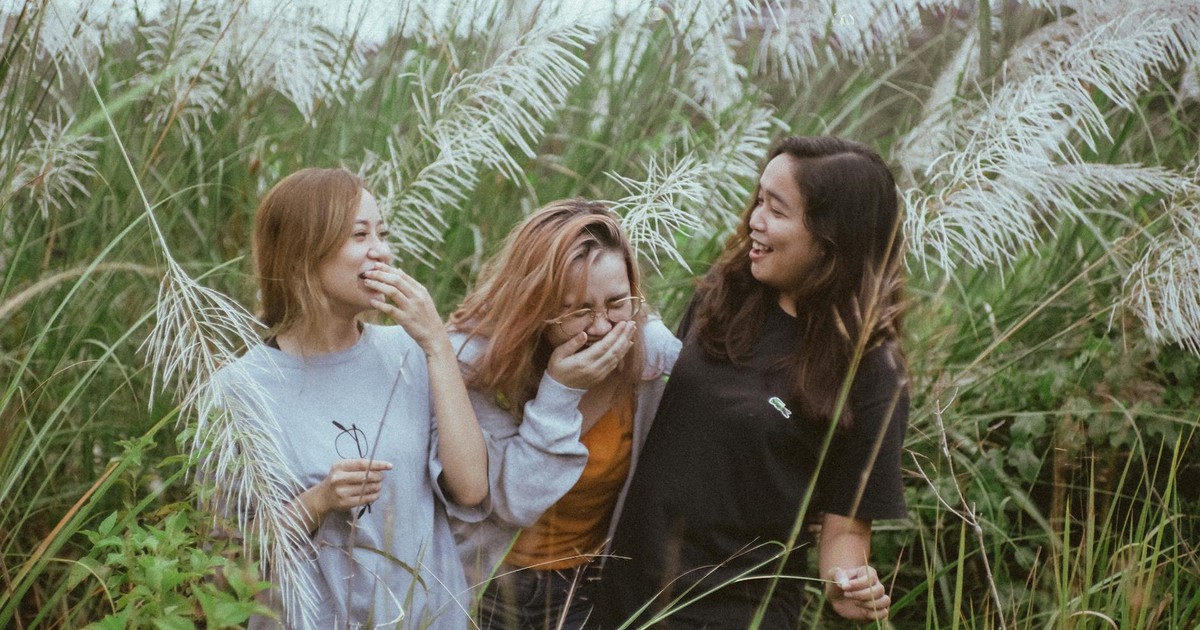 Three women enjoying a lighthearted moment amidst tall pampas grass in a natural outdoor setting.