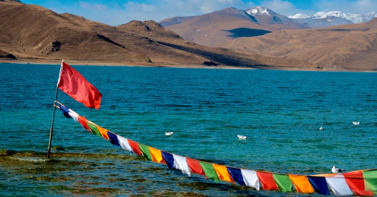 Colorful prayer flags and a serene lake in Tibet's majestic landscape.