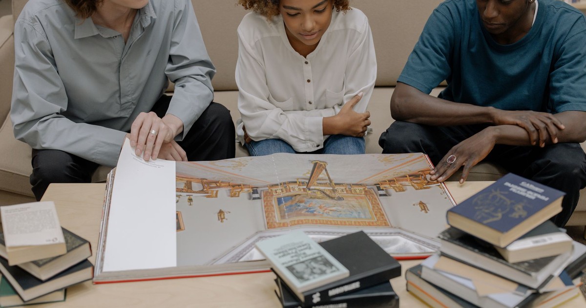 A diverse group of young adults studying together with books open on a table.