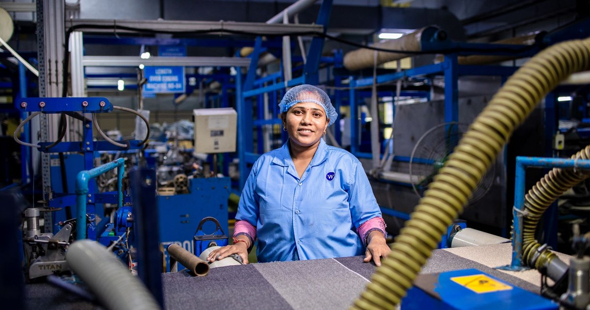 Female factory worker operating textile machinery in an industrial setting.