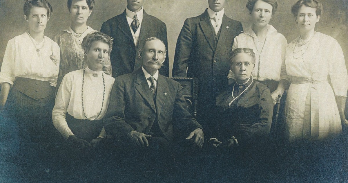 Retro family portrait with seven adults in early 1900s attire.