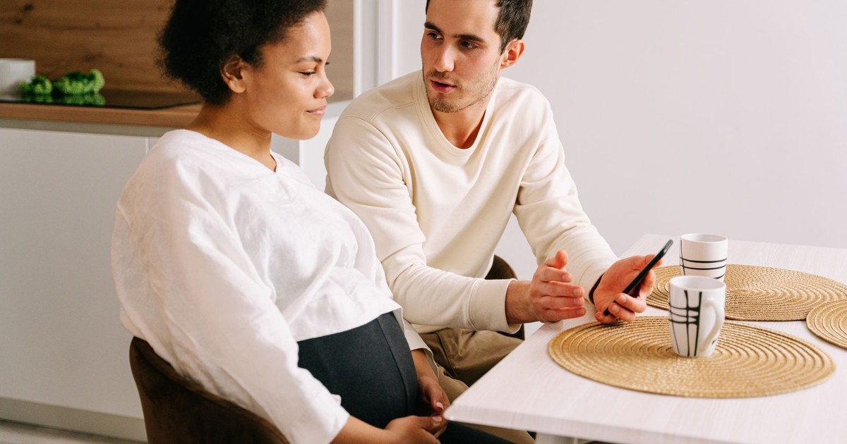 An interracial couple having a discussion about pregnancy while sitting at a kitchen table.