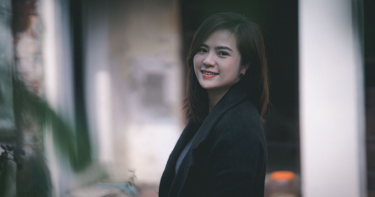 A woman stands outdoors, smiling warmly, in a black coat.