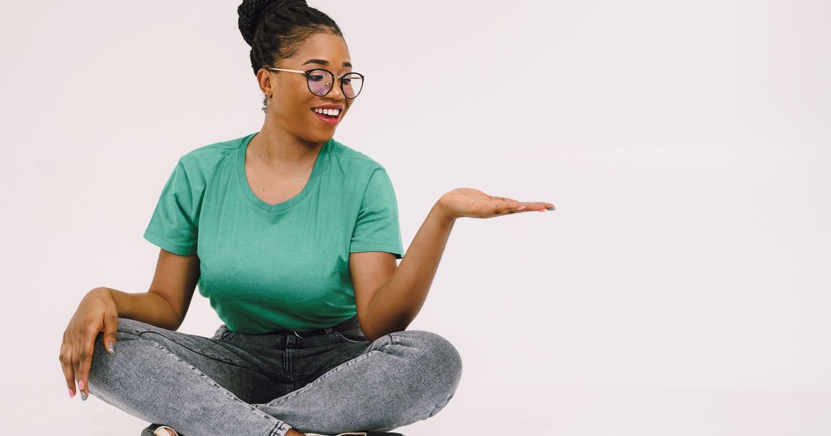 Cheerful woman in glasses sitting cross-legged and smiling.