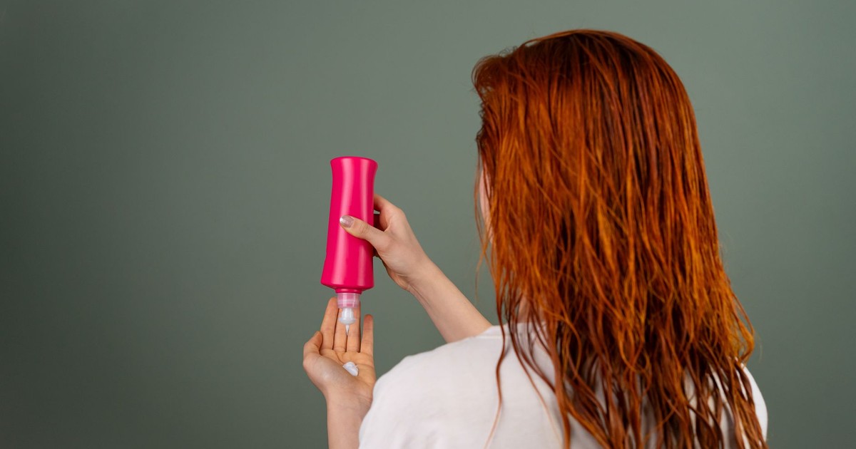Adult woman with wet red hair applying conditioner. Hair care routine.