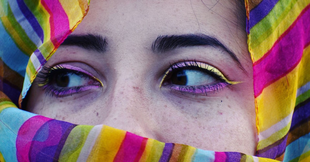 Close-up view of a woman's eyes surrounded by a colorful veil, showcasing vibrant makeup.