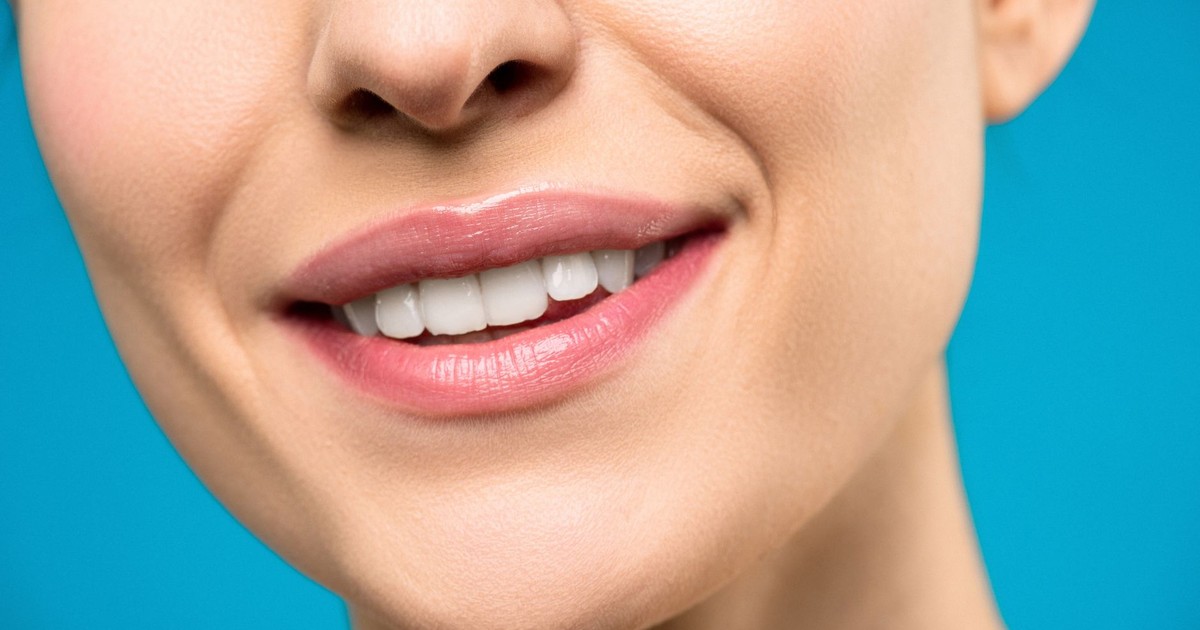 A close-up image of a woman's smile with pink lipstick and white teeth against a blue background.
