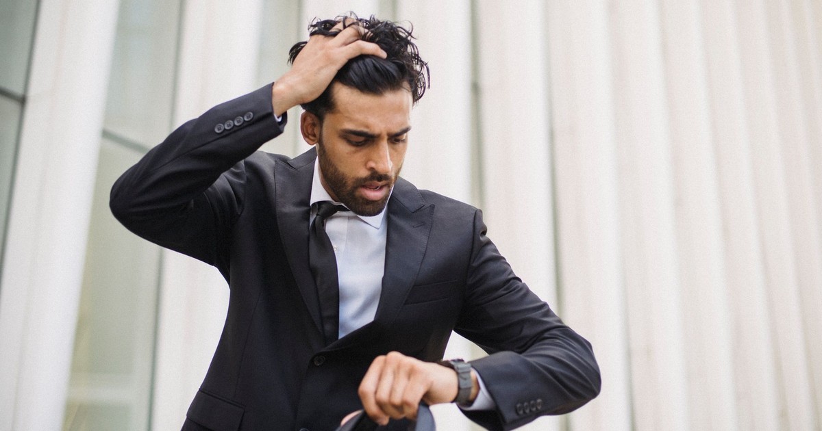 A businessman in a suit checks his watch, expressing stress. Suitable for business themes.