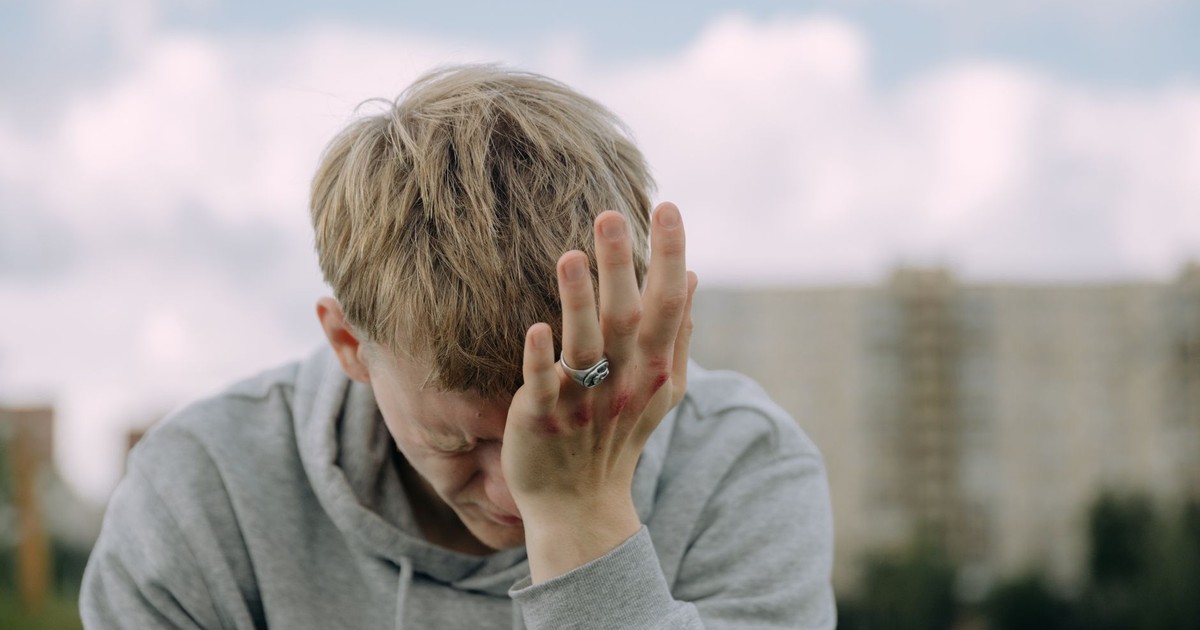 A young man outdoors holding his head in stress, depicting mental health challenges.