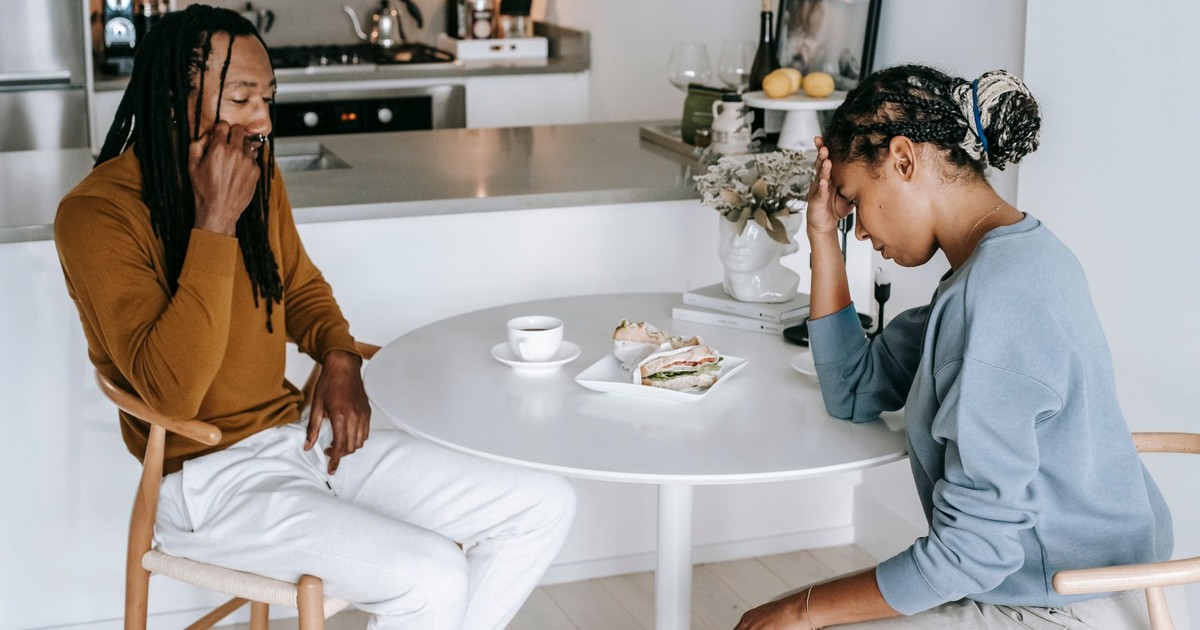 Young black female sitting at table with male and having argument while looking down thoughtfully