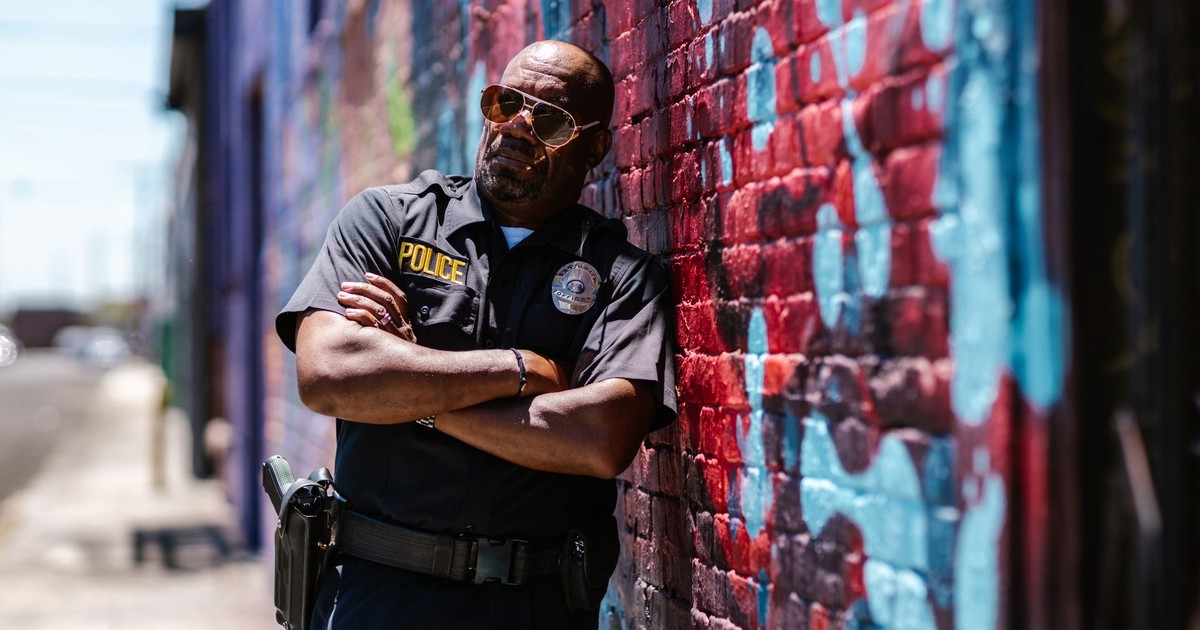 A police officer in sunglasses leaning against a vibrant graffiti wall.