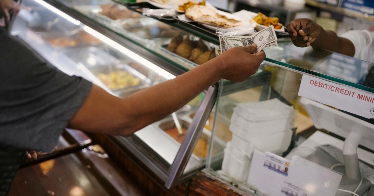 Crop faceless person standing near checkout buying food and passes money for dinner in cafe