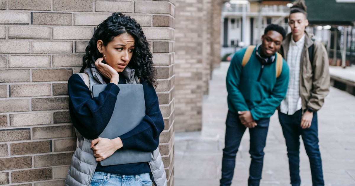 Latin American woman leaning on brick wall while hiding from multiracial classmates in college