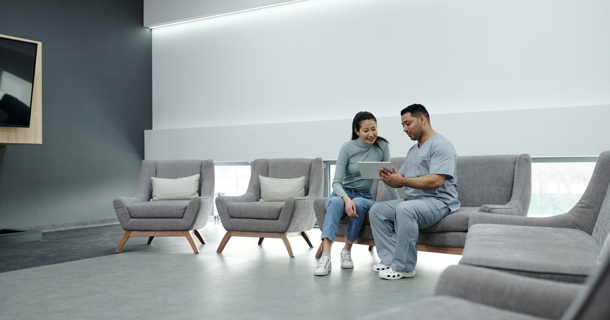 A doctor in scrubs consulting with a patient in a modern, indoor waiting area.