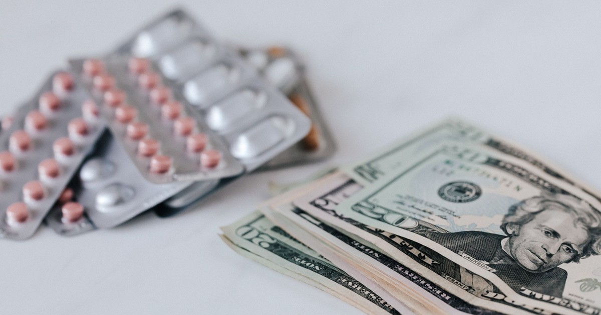 Heap of similar American dollars in cash placed near blisters of expensive drugs on white table