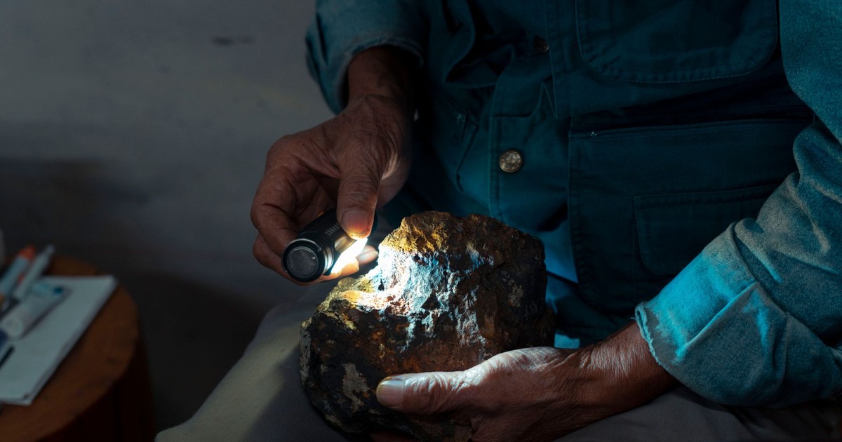 Detailed close-up of hands using a flashlight to examine a geological stone indoors.