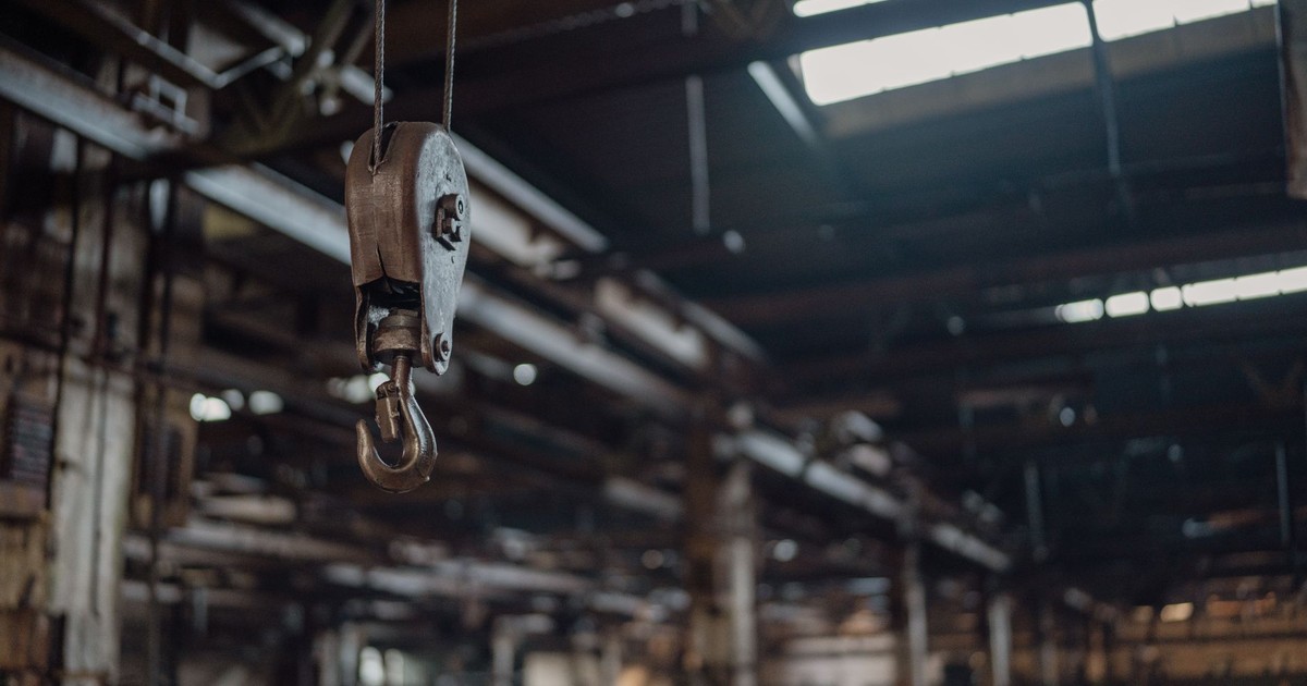 A detailed view of an industrial metal hook hanging inside a rustic warehouse.