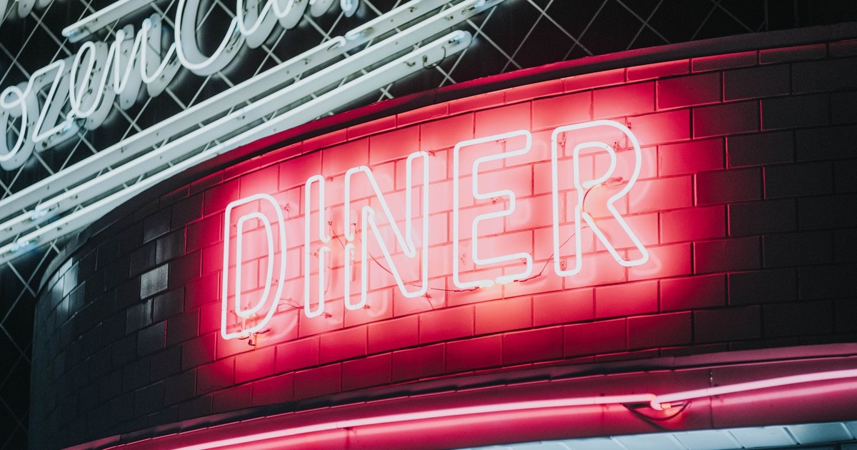 Bright neon diner sign glowing against dark tiled wall, evoking a vintage retro vibe.