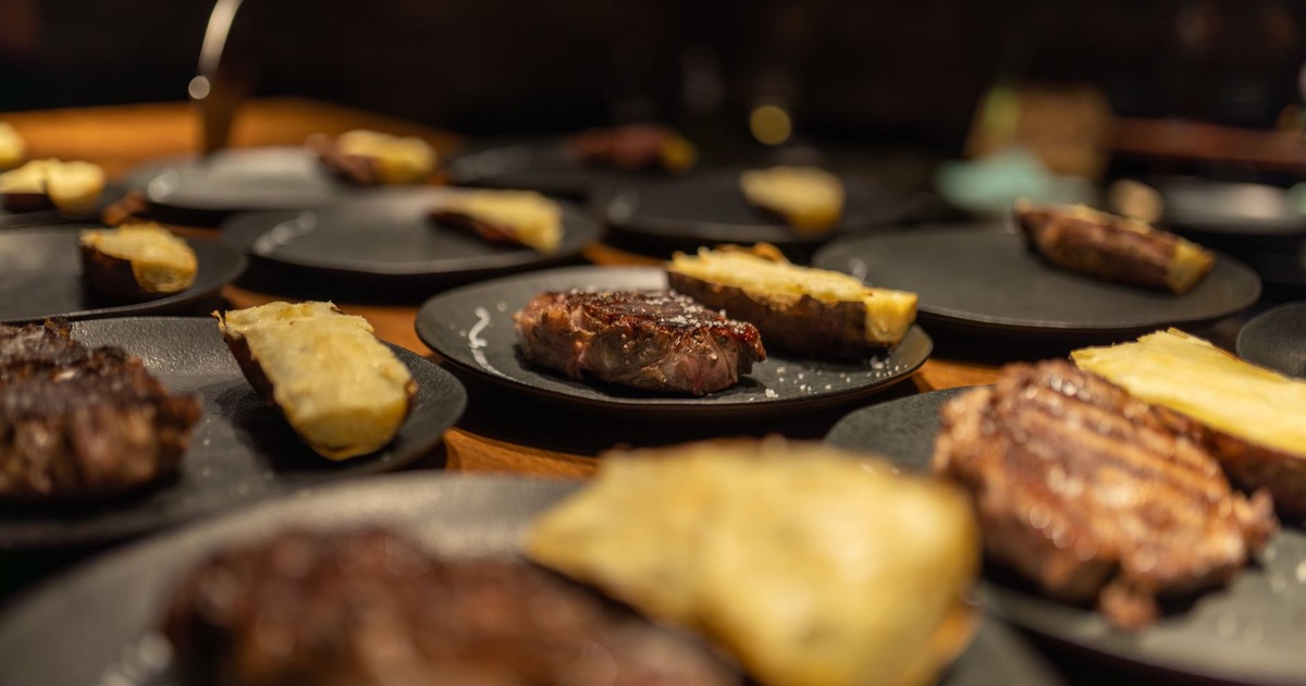 Close-up of grilled steaks with baked potatoes on black plates, warm lighting.