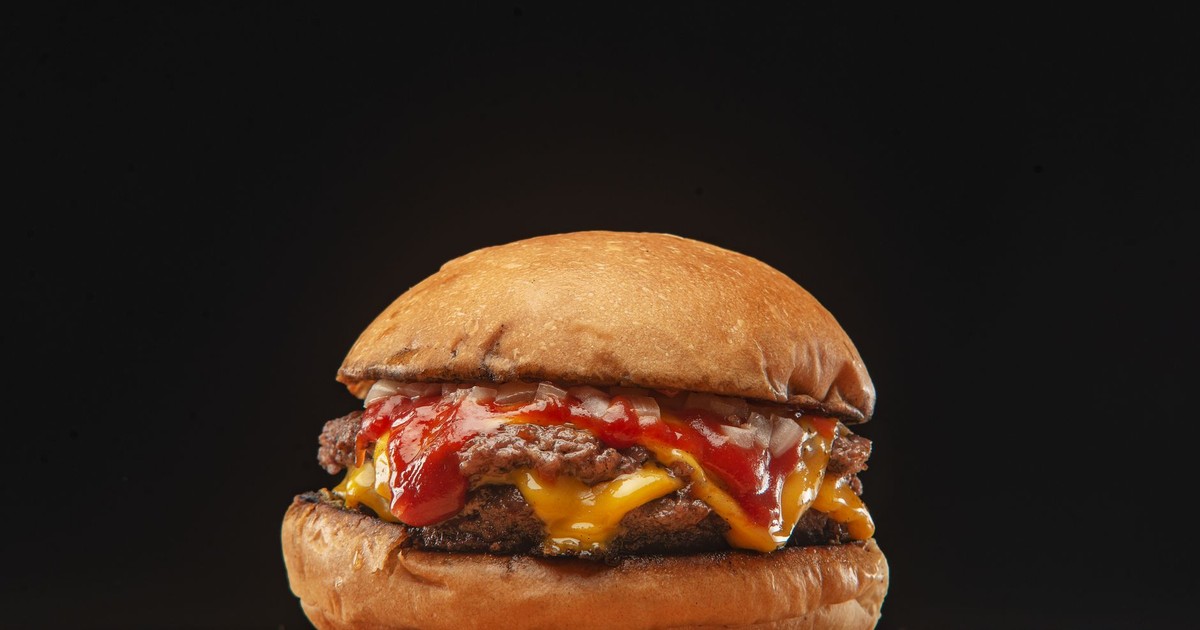 Delicious cheeseburger with melted cheese and ketchup on a black background, highlighting food presentation.