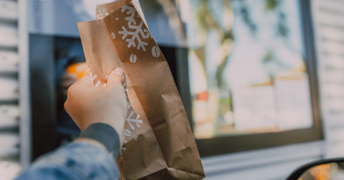 Hand reaching out with brown paper bag at drive-thru window, showcasing casual takeout.