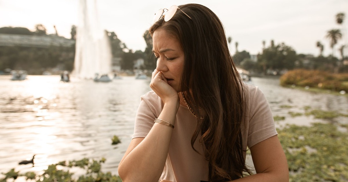 A thoughtful woman sits by a fountain, reflecting near a lake.