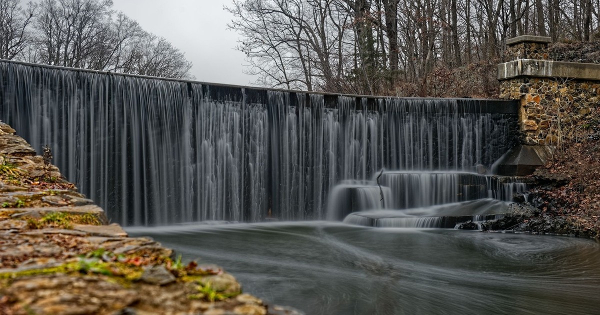 Serene waterfall flowing over stone dam in New Jersey park surrounded by bare winter trees.