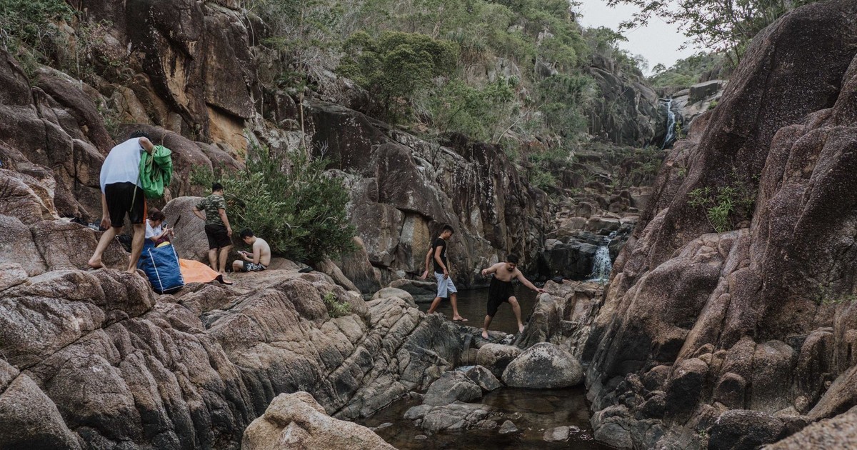 A group of people hiking and relaxing in a scenic rocky canyon with waterfall backdrop.