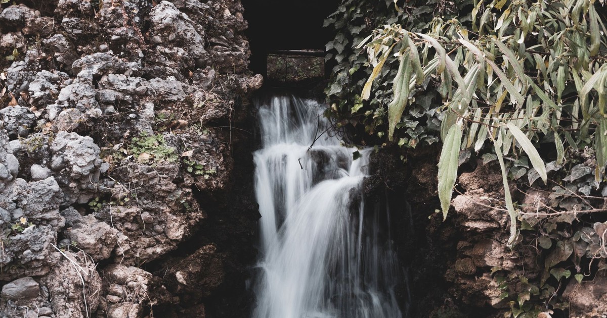 A tranquil waterfall cascades over rocky terrain surrounded by lush greenery.