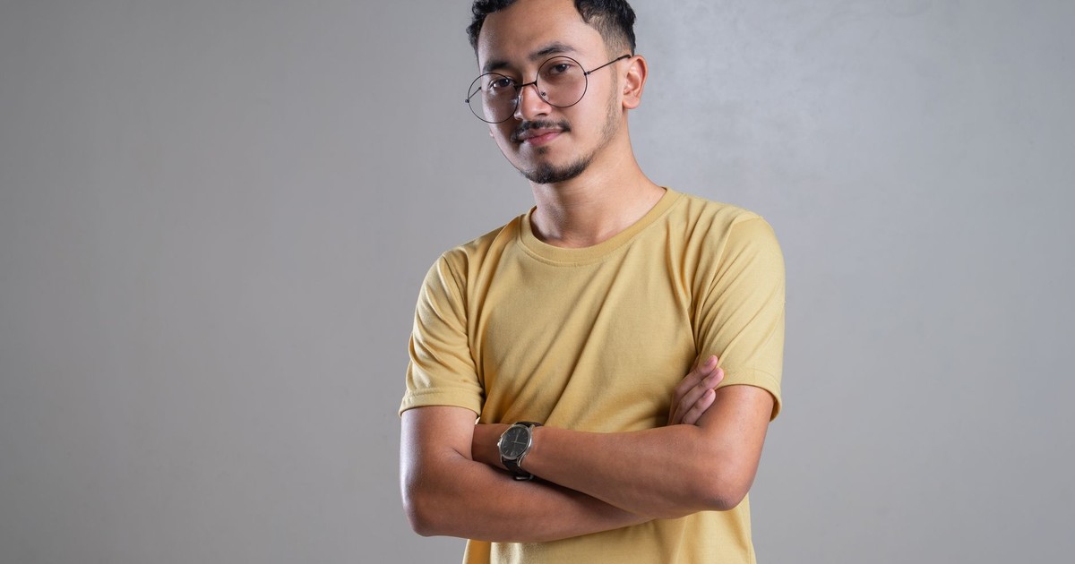 Portrait of a young man with eyeglasses and a confident pose in a neutral setting.