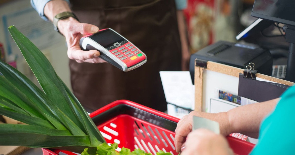 A customer using a contactless payment method at a grocery store checkout with fresh produce.