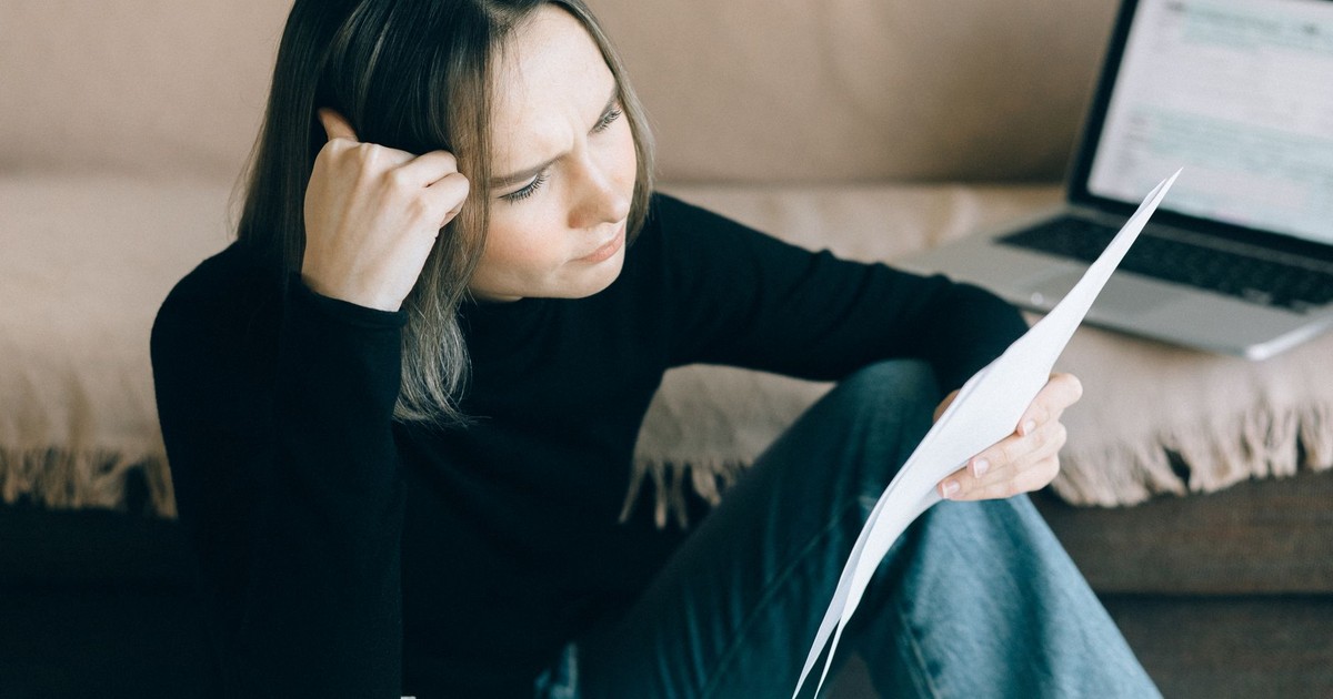 Focused woman analyzing papers with a laptop open, symbolizing thoughtful consideration.