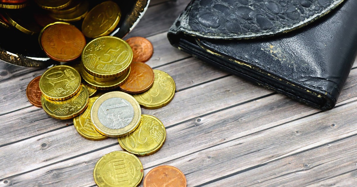 A worn-out leather wallet and scattered euro coins on wooden surface suggest economic hardship.