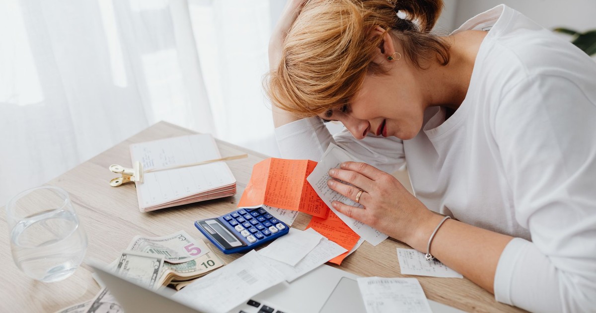 A woman overwhelmed with finances, surrounded by bills, calculator, and cash at home.