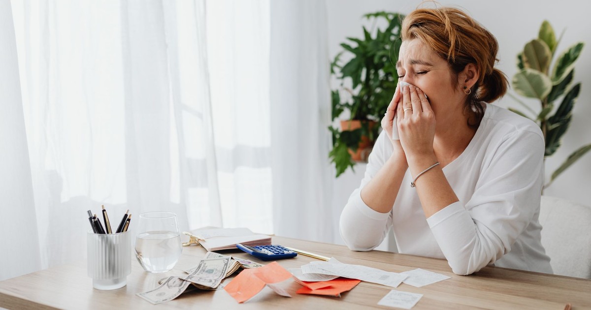 Woman looking stressed while managing finances at her office desk with papers and calculator.