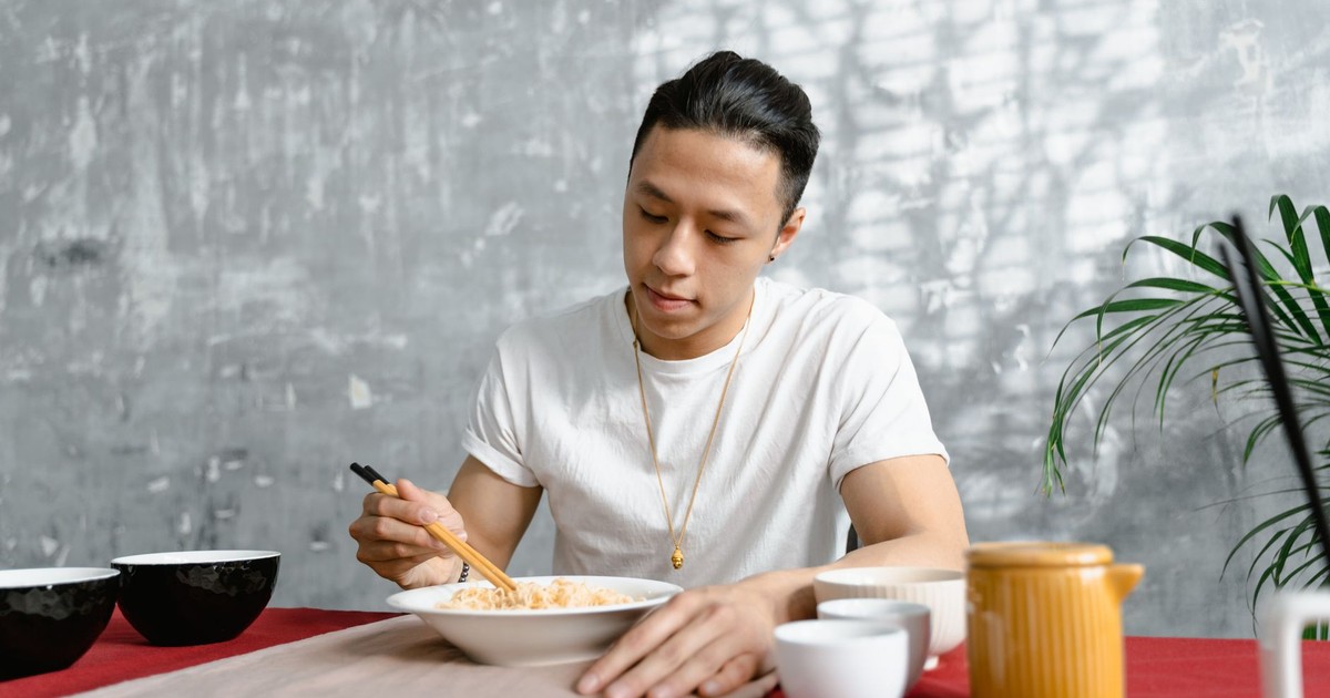 An adult man uses chopsticks to enjoy a delicious meal indoors, exuding a calm and relaxed vibe.