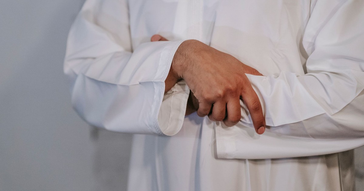 A close-up image of a man's hands in a traditional Islamic thobe indoors, symbolizing cultural identity.