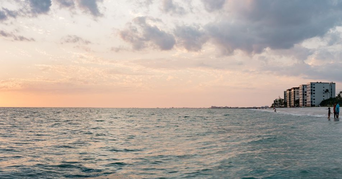 Panoramic view of a sunset over the ocean with beachfront buildings and people on the shore.