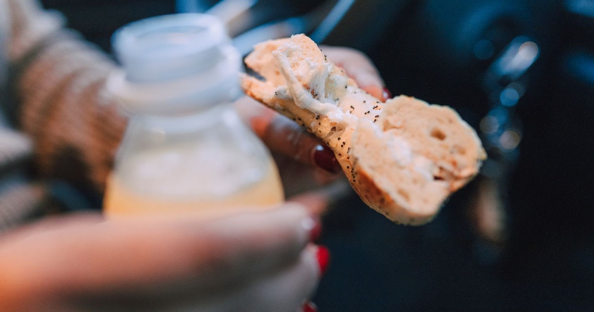 Close-up shot of a hand holding a bagel and a drink bottle inside a car, perfect for lifestyle themes.