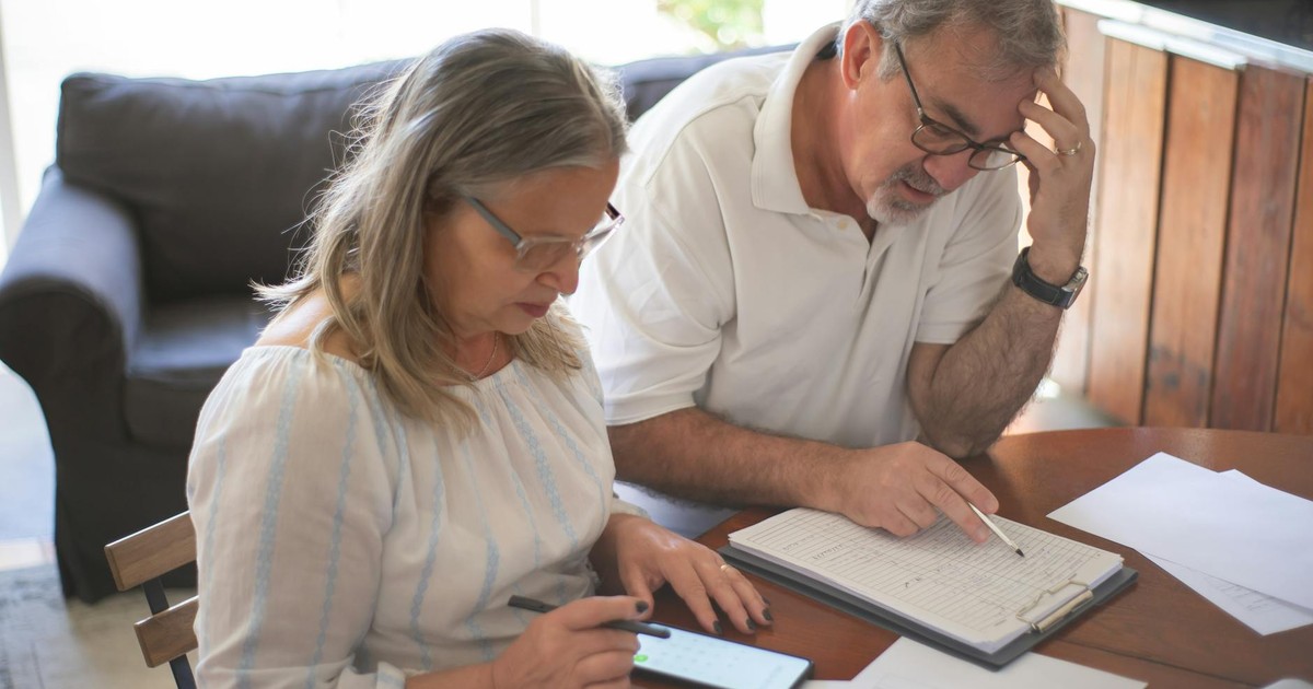 Elderly couple reviewing bills and documents at home, focusing on finances and technology.